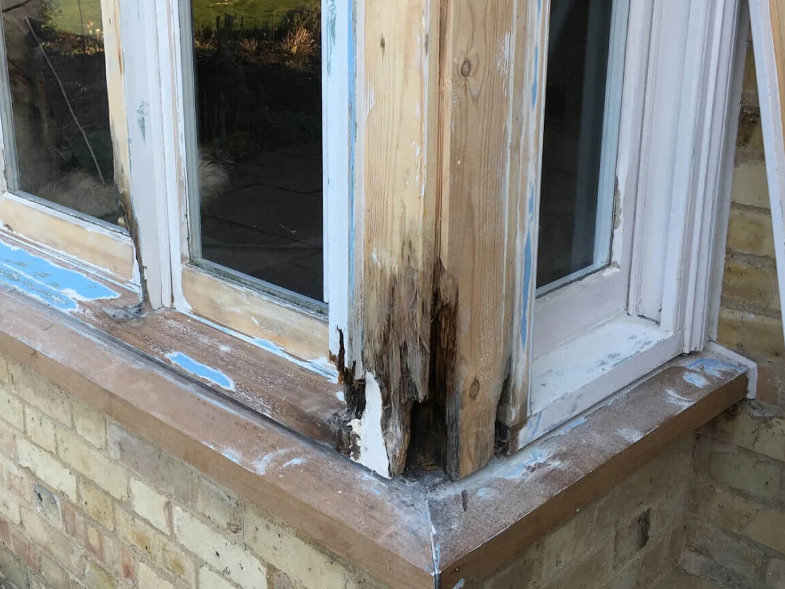 Timber sash window before restoration, with flaking paint and decayed sill