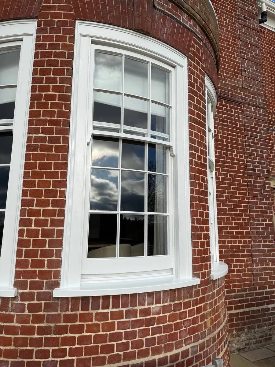 Restored white multi-pane sash window with astragal bars set in a curved red-brick bay turret