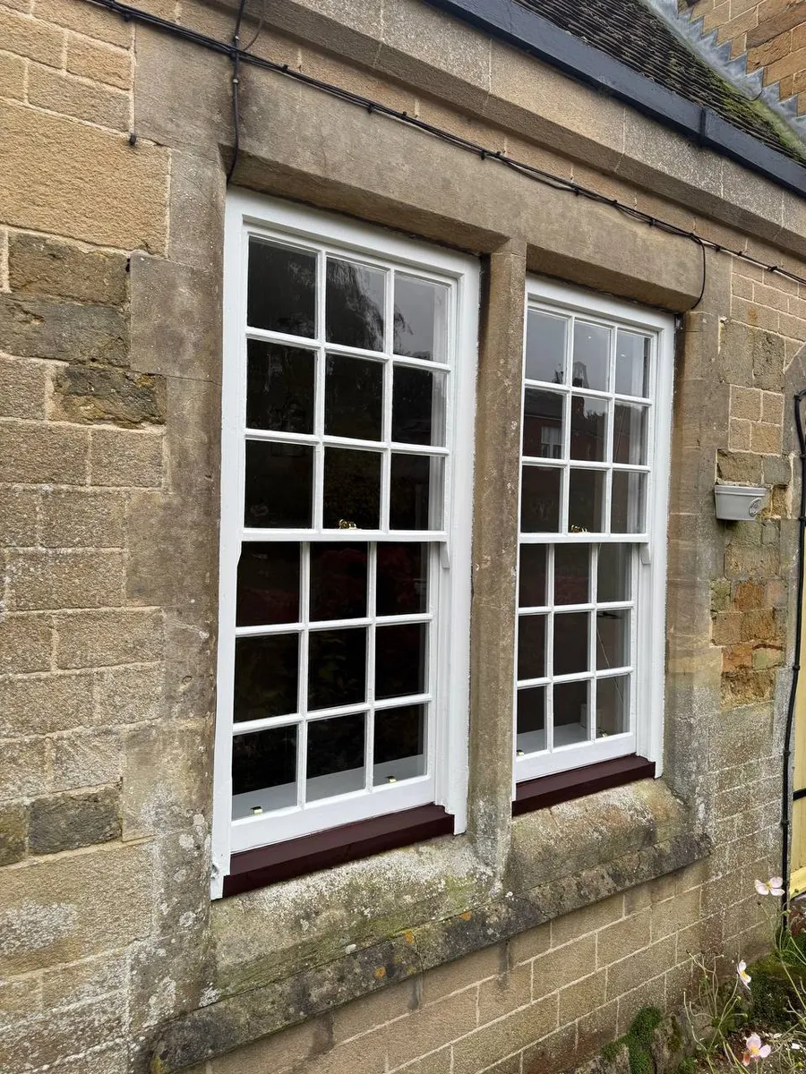 Restored Georgian sash windows with white frames on a stone cottage
