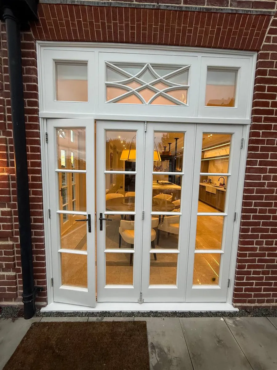 White timber french doors with glazing bars and a decorative fanlight opening onto a warmly lit kitchen-diner