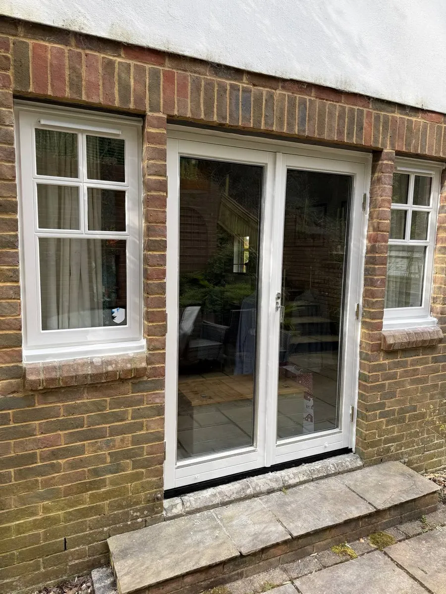 Restored white timber french doors with two side casement windows on a brick house