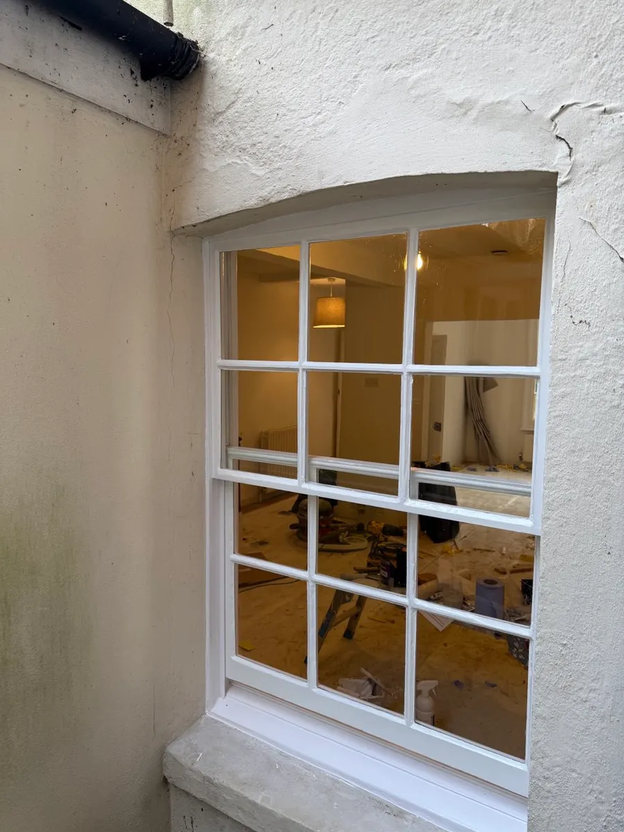 Freshly restored white timber sash window with arched head in a period rendered wall